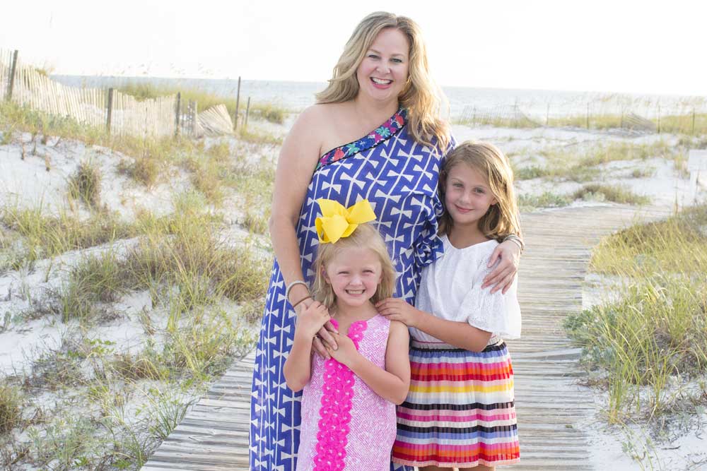 adrianne graves in dress standing on beach with two young daughters