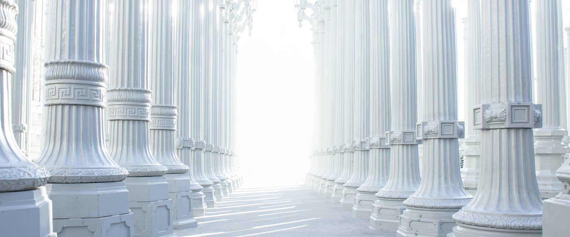 many rows of white pillars with bright white light in the distance