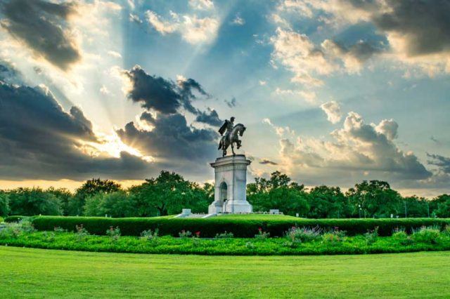 hermann park statue in houston with sun peeking through clouds in the sky