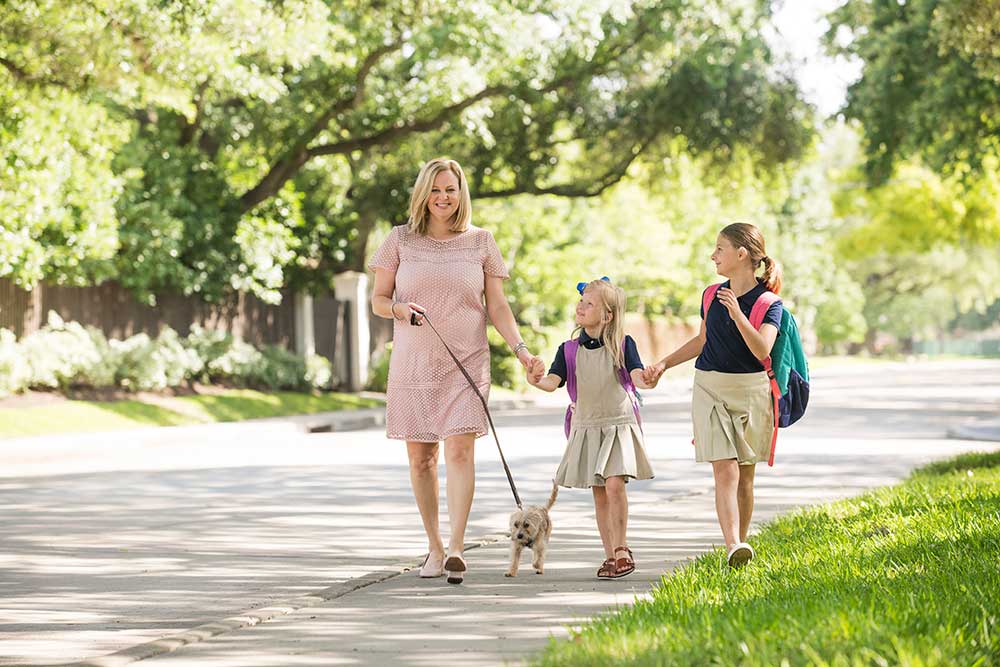 adrianne graves walking dog with two daughters along street with trees